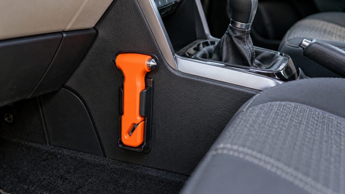 An orange escape hammer and protected belt cutter sit in a cradle beside a car’s centre console.