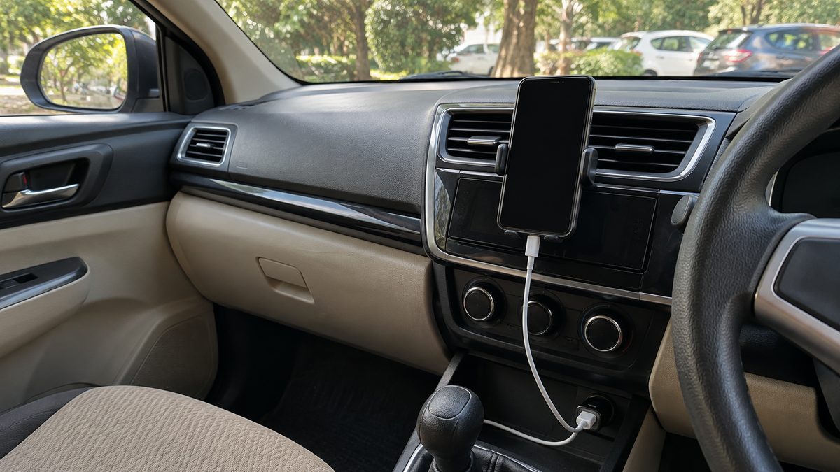 A mounted phone with a dark screen connected to a charger in a parked car’s centre console.