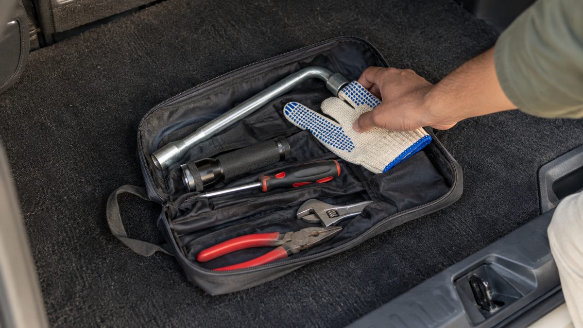 A hand checking a compact tool pouch with a wheel wrench, gloves and torch in a car boot.