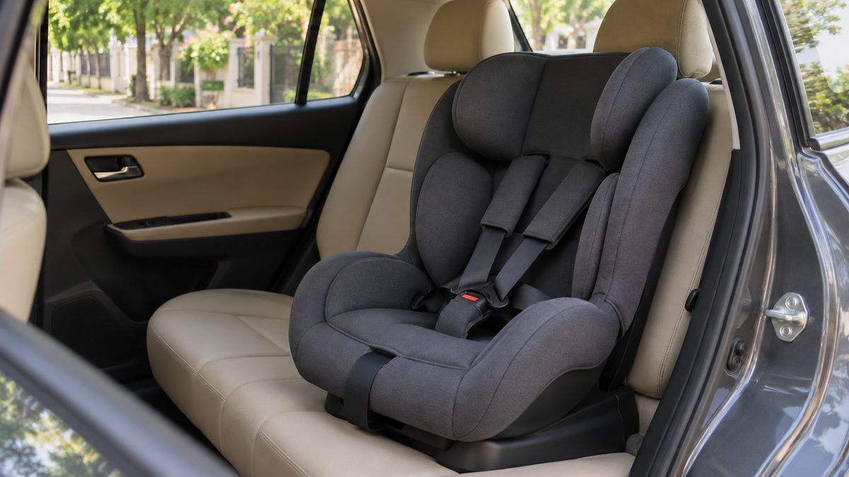 Empty charcoal child safety seat with a five-point harness on a beige rear bench beside an open car door.