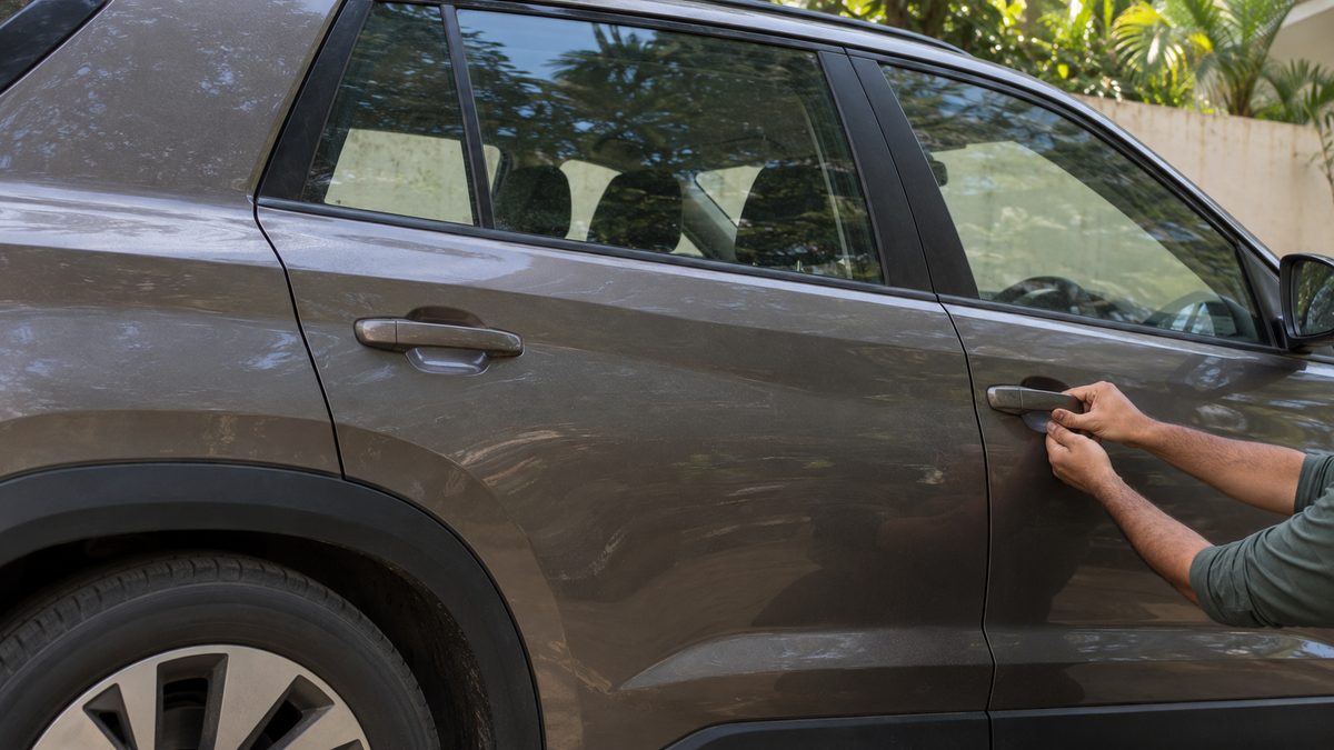 Hands checking the door handle of an unbranded SUV in a residential parking area in India.